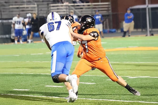 Two football players make contact during a game on a lit field at night.