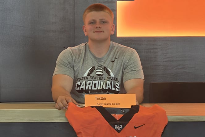 Person seated at a table behind a name card reading “Tristan” and “North Central College.” The person is wearing a gray North Central College Cardinals T-shirt, with an orange football jersey displayed on the table in the foreground.