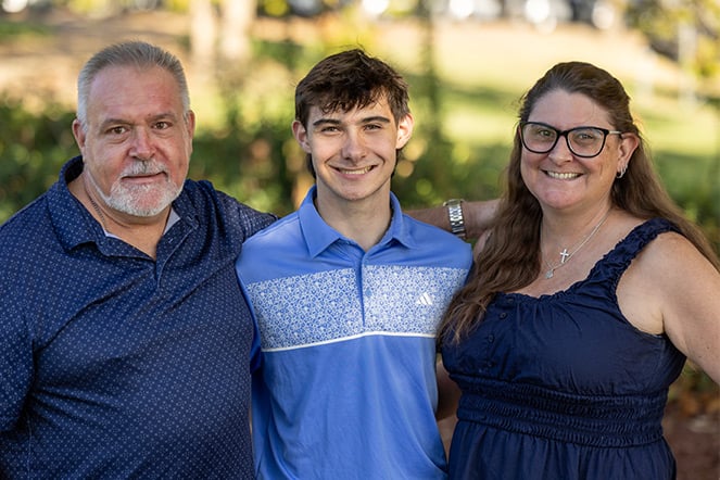 Outdoor family portrait featuring three people standing close together with their arms around one another.