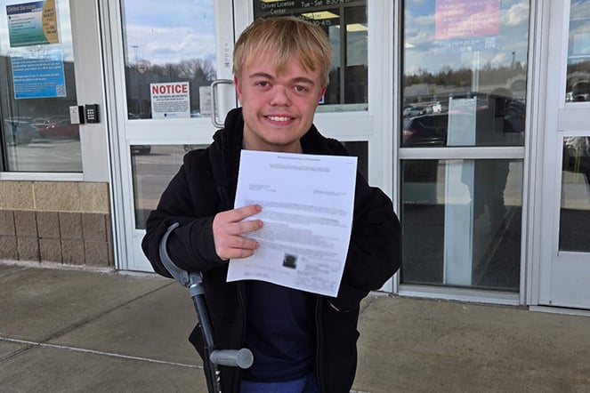 a teenager holding up a piece of paper outside of a building
