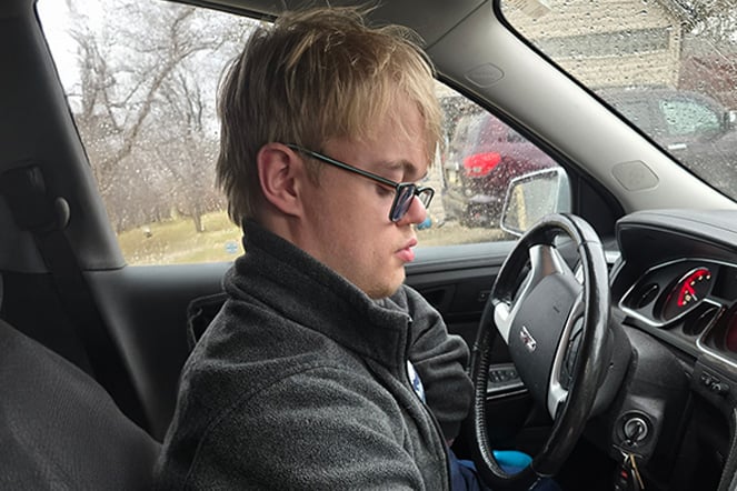 a teenager with glasses driving a car in the rain