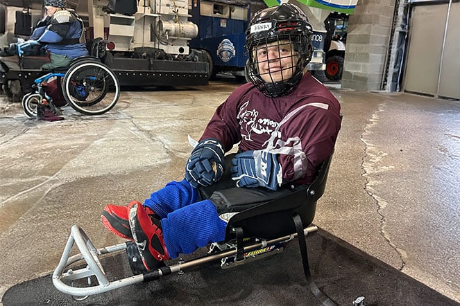 a teenager in a hockey uniform and helmet in a sled used for hockey
