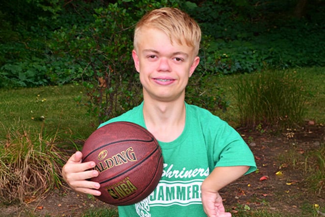 a teenager holding a basketball in front of a forest