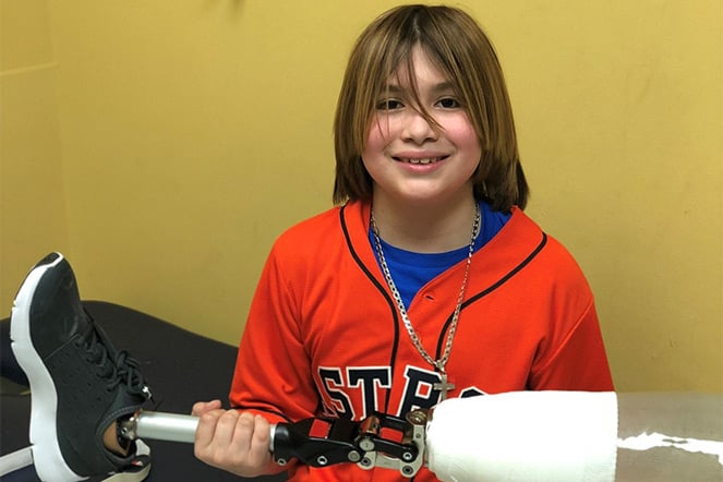 Adison sitting on exam table holding her leg prosthetic
