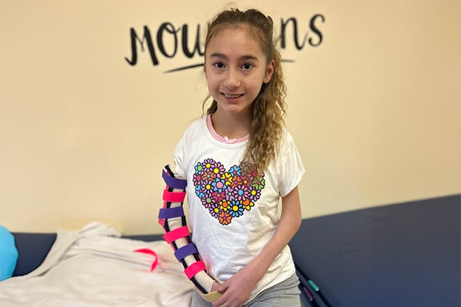 a young child with a colorful arm brace smiling on an examination table 
