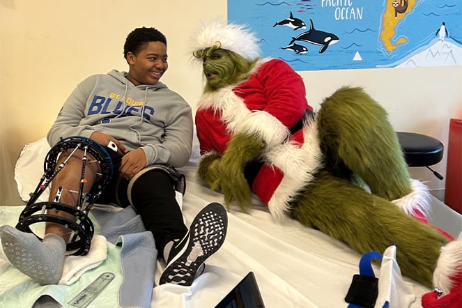 a teenager with a leg lengthening device smiling and laughing with a person dressed as The Grinch
