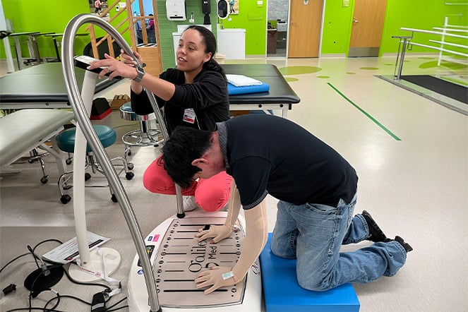 a teenage kneeling on the ground while using their hands to push himself up in a physical therapy room