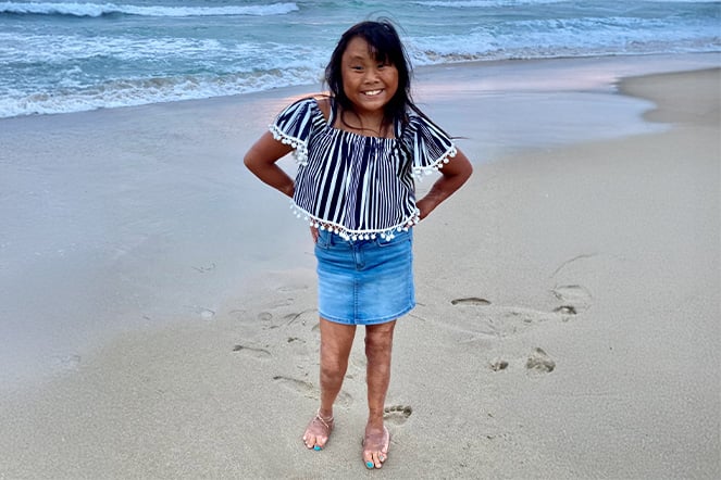 a child standing and smiling on the shoreline of a beach