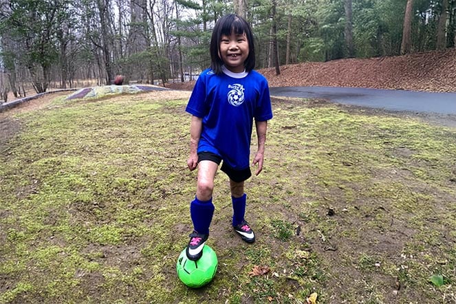 a child dressed in a soccer uniform with her foot on a soccer ball