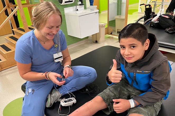 a child giving a thumbs up next to a smiling woman in hospital scrubs