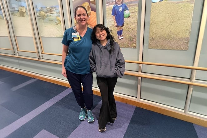 a woman dressed in hospital scrubs stands next to a child in front of a row of large photos