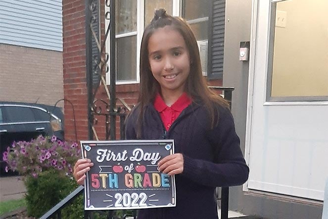 Casence standing outside hilding a First Day of School sign