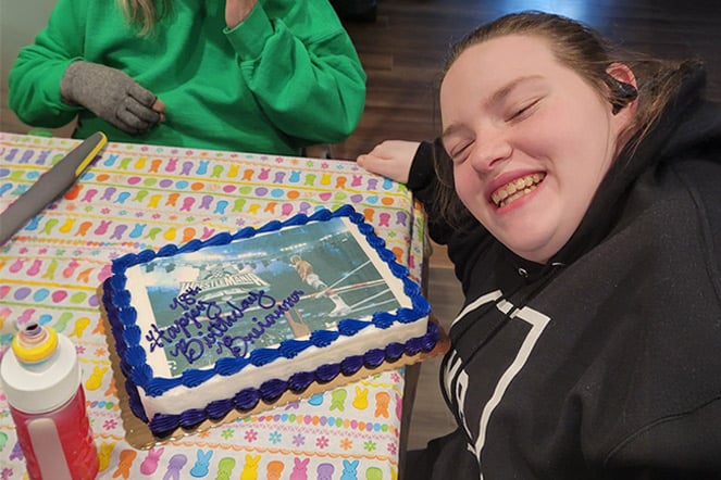 Cerebral palsy patient leaning and smiling over a cake that reads "Happy 18th Birthday, Brieanna"
