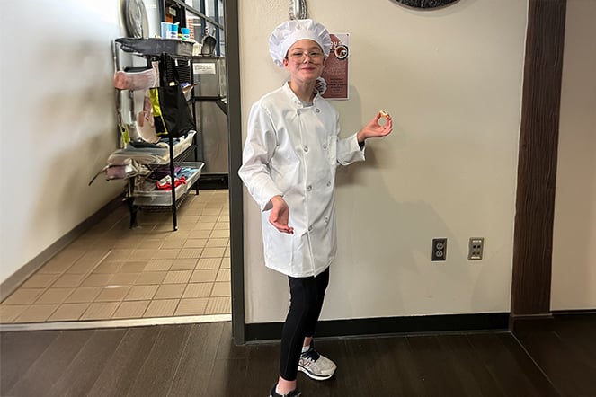 a child dressed in a chef uniform outside of a restaurant kitchen