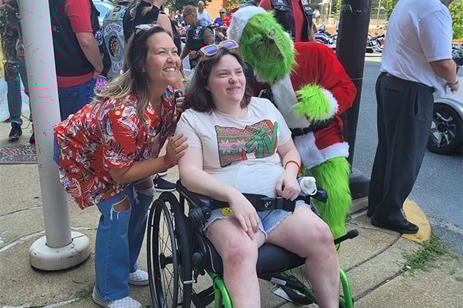 cerebral palsy patient smiling with an adult and a person dressed as the Grinch at a parade