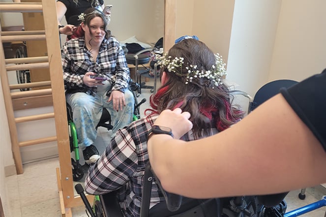 Cerebral patient in a wheelchair looking in a mirror while an adult curls their hair