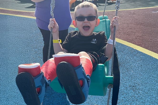 a laughing child with two leg casts on a swing set