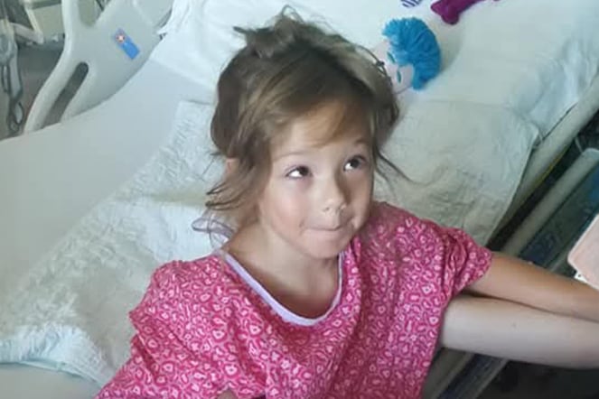 a young child smiling and wearing a hospital gown 