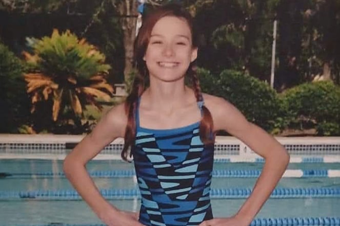 a child wearing a swim team uniform smiling in front of a pool