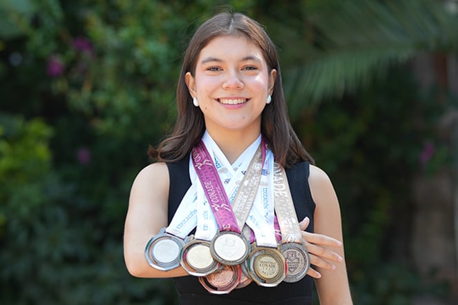 a smiling teenage woman showing off her collection of award medals around her neck