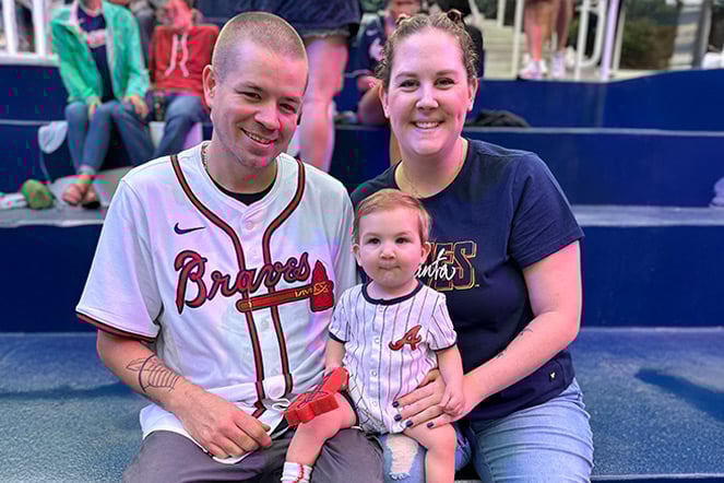 two parents holding an infant at a baseball game