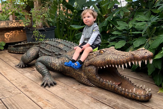 a toddler sitting on a bronze statue of a life-sized alligator