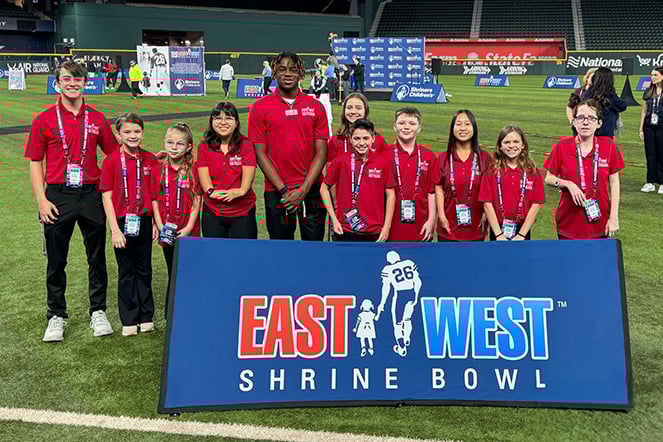 Elevent patient ambassadors in matching shirts surrounding a banner that reads "East West Shrine Bowl"