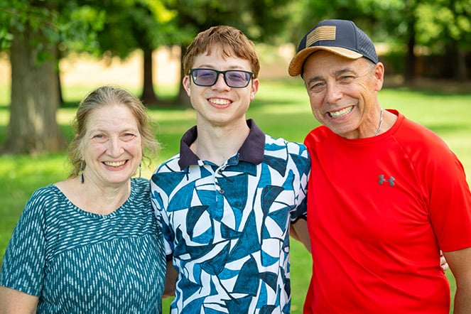 a teenager wearing sunglasses standing with two older adults