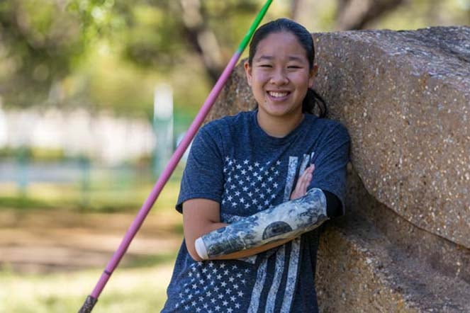 Danielle leaning on rock, javelin in background