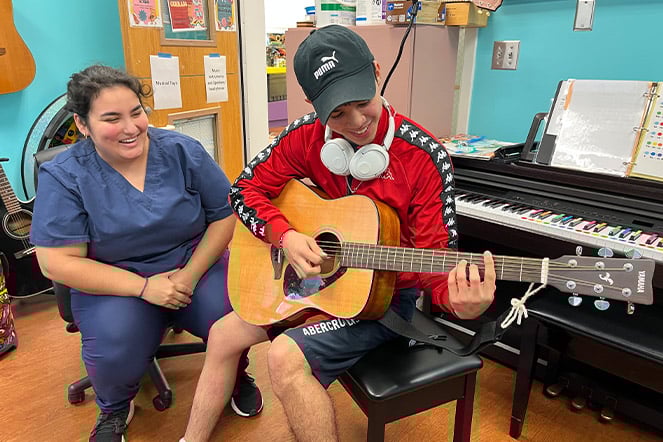 Elian plays guitar while Angie watches on.