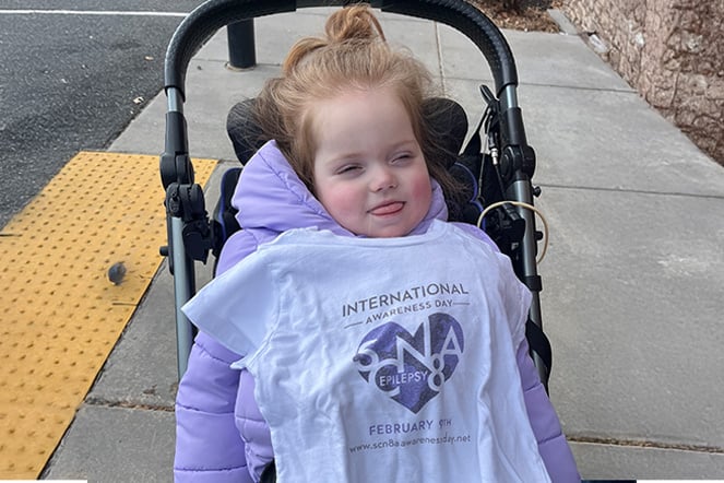 a smiling child with a t shirt draped over them that reads "International 5CN8A Epilepsy Awareness Day"