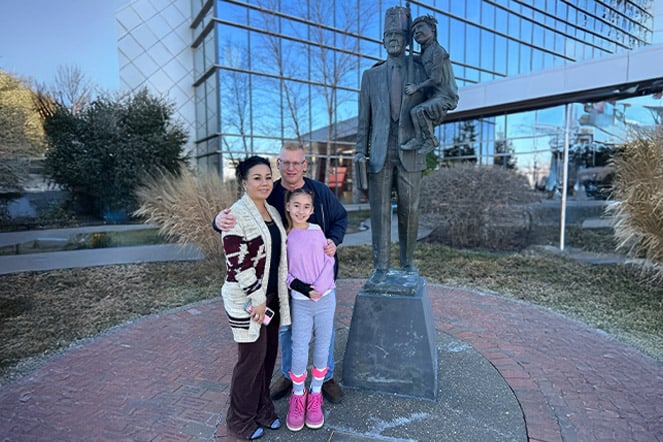 a family smiling outside next to a large bronze statue