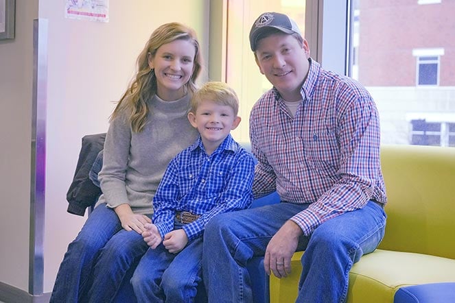 a family of three seated in front of a window smiling at the camera