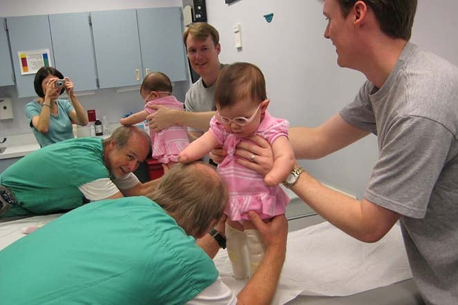 Grace being fitted for her first prosthetic legs, provider and father assit, mom takes photo