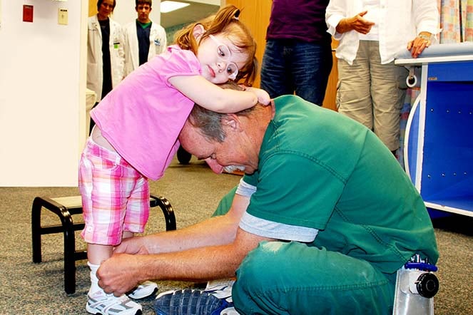 Grace leaning on prosthetic provider while he adjusts her prosthetic legs