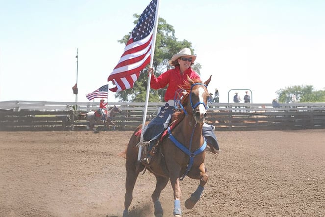 Female riding a horse holding an American flag