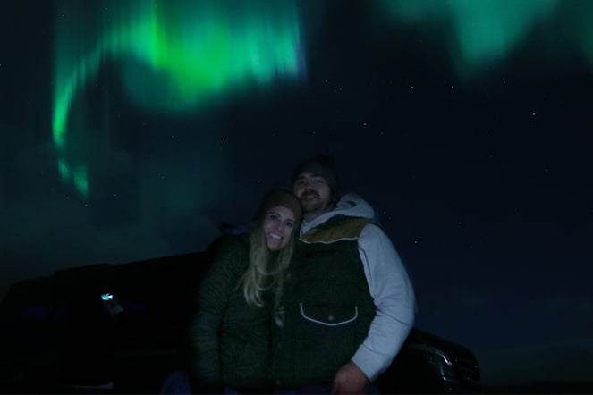 a man and a woman standing in front of an aurora borealis 
