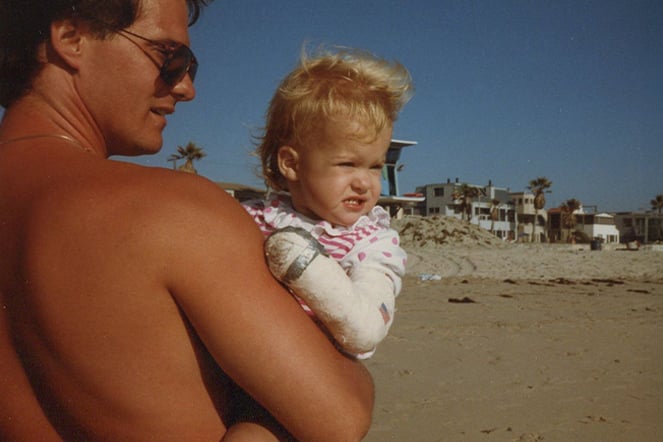 a vintage photo of a man holding an infant with an arm cast on a beach