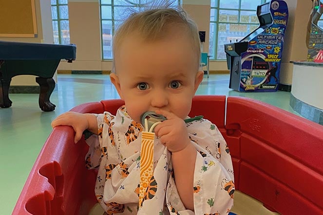 Kohen sitting in a little red wagon with pacifier in mouth