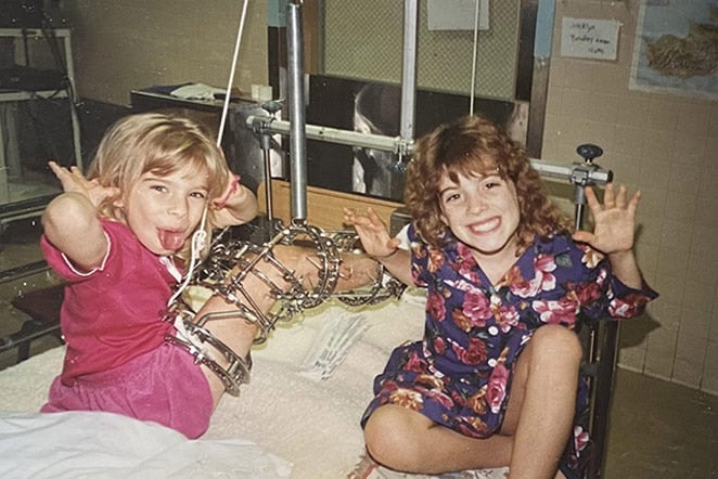 patient with leg brace on hospital bed with sister making funny faces