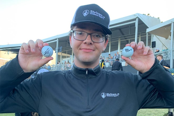 a young man holding up two golf balls at a golf tournament
