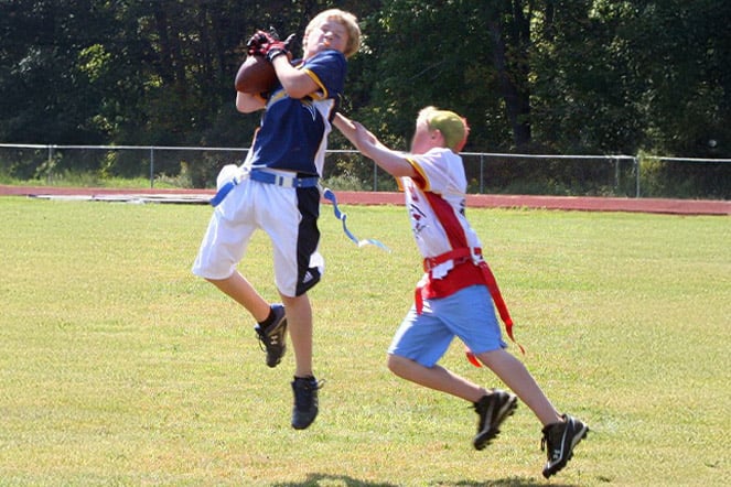 two children playing flag football, one of them is jumping and catching a football