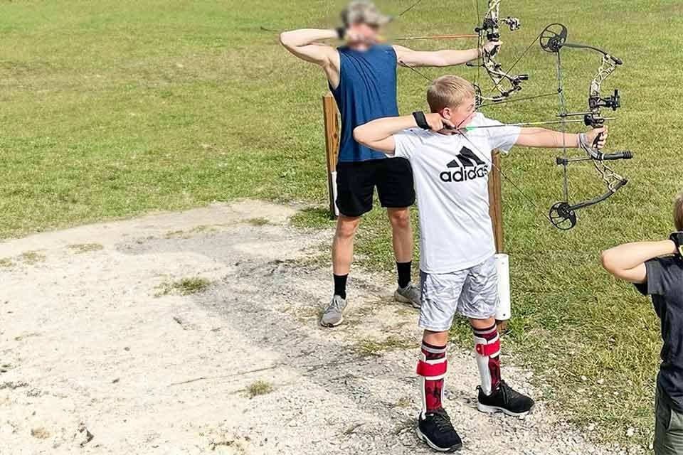 Patient in leg braces practicing archery with friends