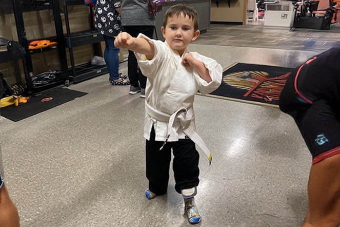 a child with a prosthetic leg wearing a traditional karate kimono strikes a pose with his fists