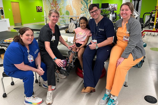  a group of physicians smiling around a happy young child wearing an external fixator