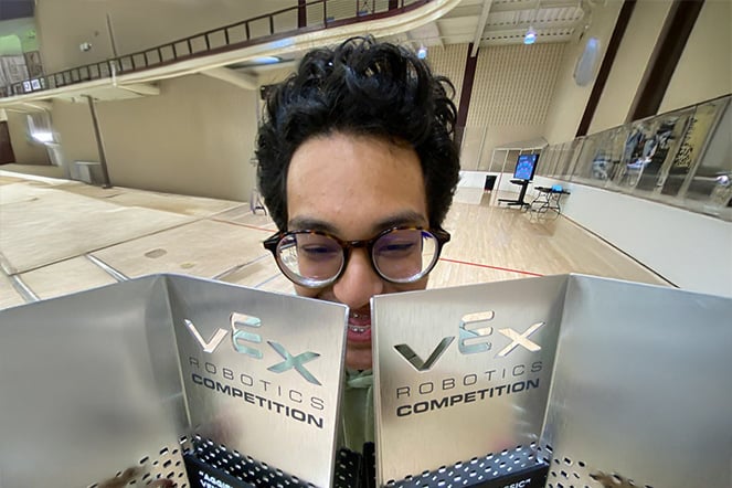 a teenager holding up two metal awards that each read "VEX Robotics Competition"