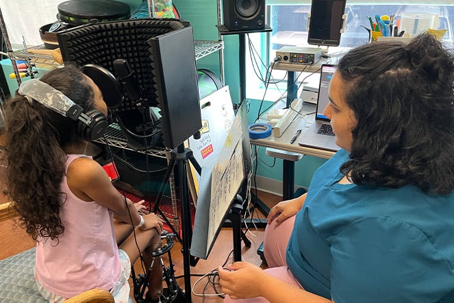 a child singing into a microphone while an adult watches on