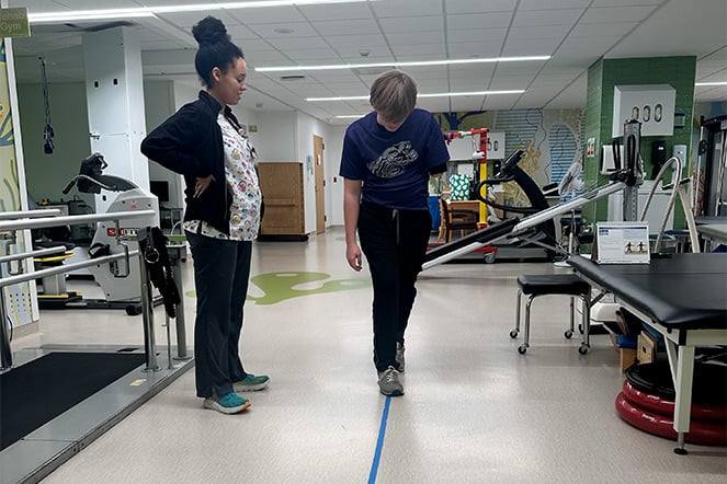 Nathanial walking a straight line on the floor during a physical therapy session with staff.