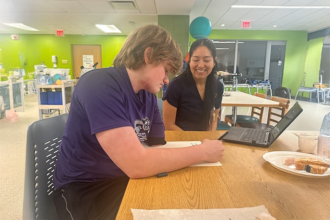 Nathanial practicing writing with his left hand with a staff member during a physical therapy session.