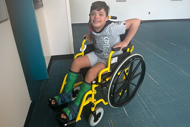 a  smiling child in a wheelchair with two casts on his feet
